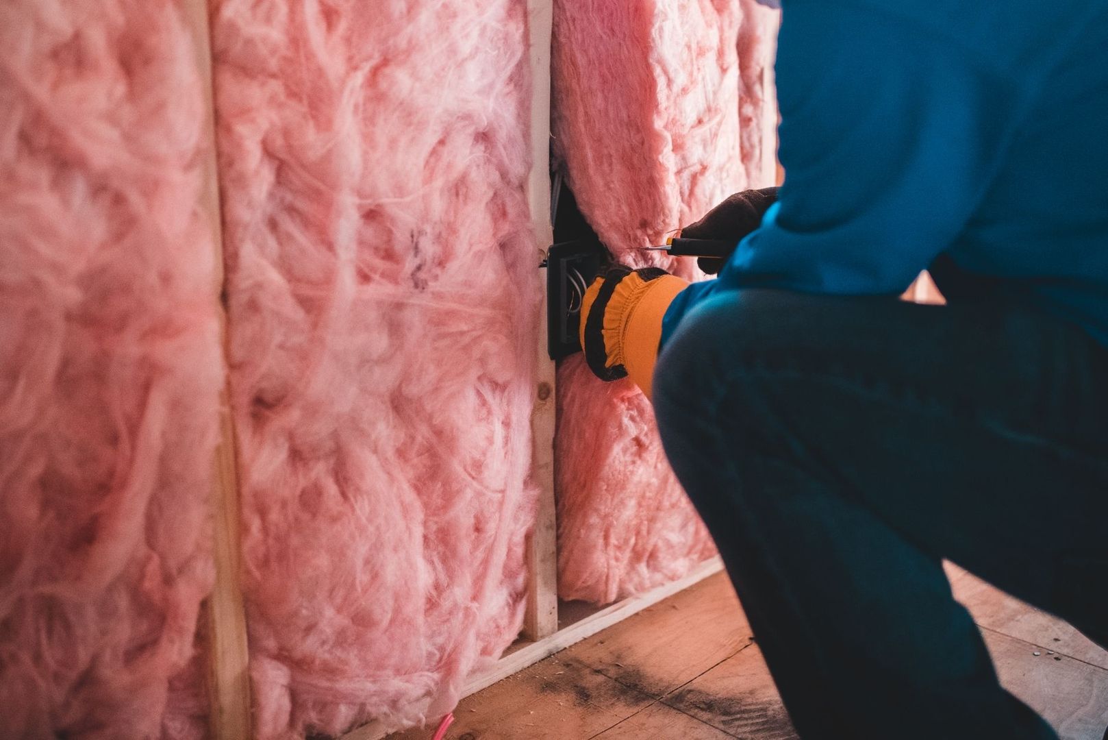 Håndverker monterer rosa mineralull mellom trestendere i en vegg