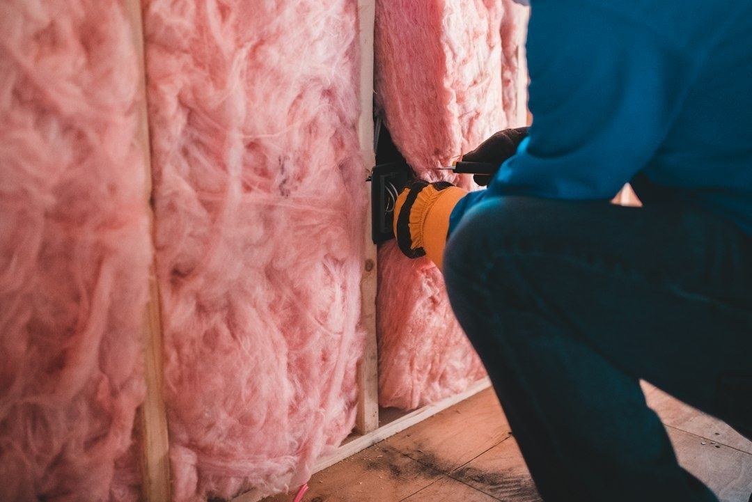 Håndverker monterer rosa mineralull mellom stendere i en vegg