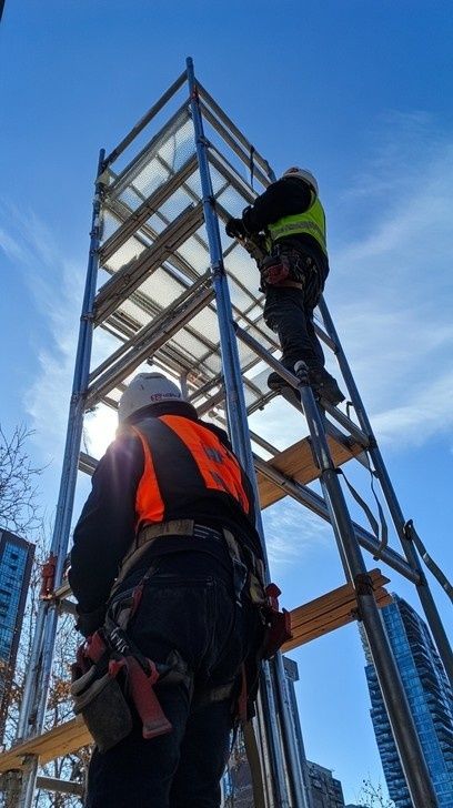 To arbeidere monterer et høyt stillas med verneutstyr